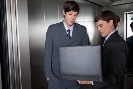 Male in suit showing something in the briefcase to his colleagueの写真素材