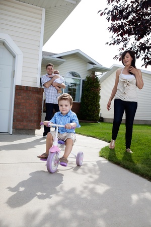 Little boy learning to ride tricycle while parents watchの写真素材