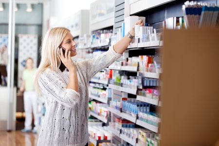 Female talking on cell phone while looking for medicines at drugstoreの写真素材