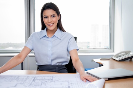 Portrait of pretty female architecture sitting with blueprints on deskの写真素材