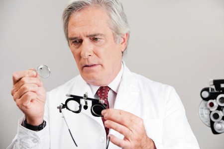 Skilled optometrist examining the lens while holding trial frame for an eye checkupの写真素材