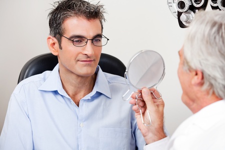 Man in stylish reading glasses while looking at mirror with optometrist in the clinicの写真素材