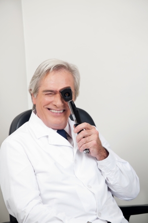Smiling mature optometrist with ophthalmoscope for an easy view at retinaの写真素材