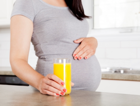 Woman in third trimester holding orange juice in kitchenの写真素材