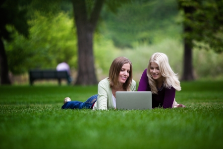 Two young happy women using laptop in parkの写真素材