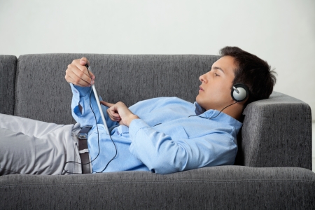 Relaxed young man in formal wear browsing internet while listening to music on digital tabletの写真素材