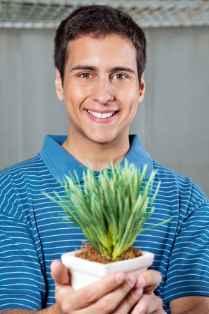 Portrait of handsome young man smiling while holding small plantの写真素材