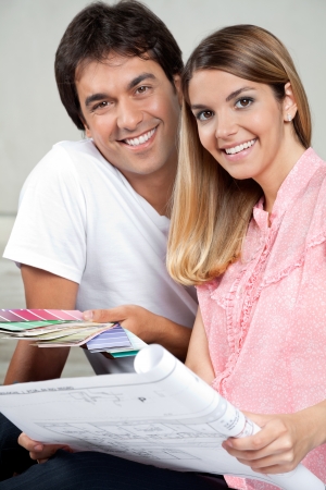 Portrait of happy young couple with blueprint and color swatchesの写真素材