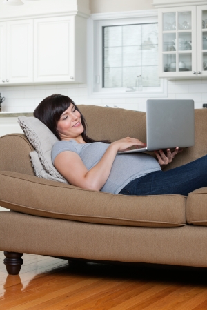 Happy pregnant woman using laptop while lying on sofaの写真素材