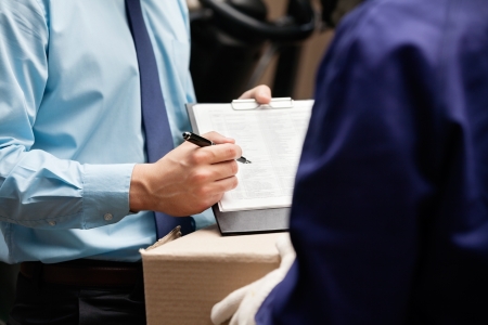 Midsection of supervisor showing clipboard to foreman at warehouseの写真素材