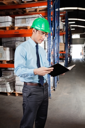 Young male supervisor reading book at warehouseの写真素材