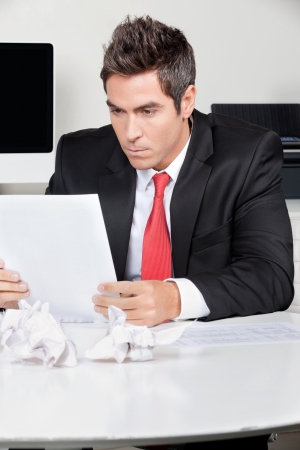 Young businessman reading document at desk in officeの写真素材