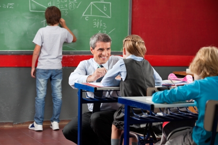 Teacher Looking At Schoolgirl While Crouching At Deskの写真素材