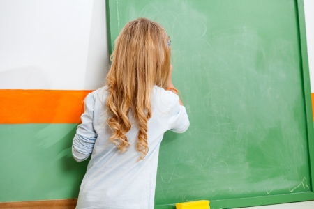 Little Girl Writing On Chalkboard In Classroomの写真素材