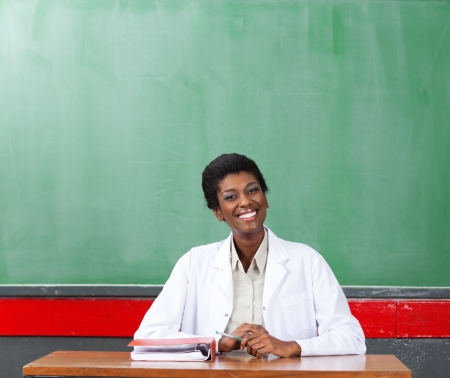 Happy Female Teacher Sitting At Desk In Classroomの写真素材
