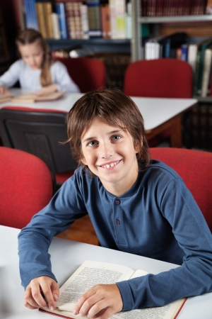 Schoolboy With Book Sitting In Libraryの写真素材