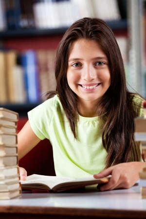 Happy Schoolgirl Sitting At Table In Libraryの写真素材