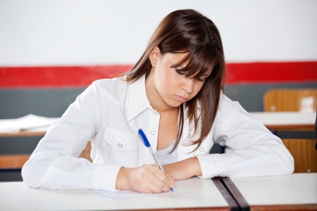 Teenage schoolgirl writing on paper during examination at desk in classroomの写真素材