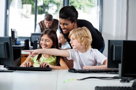 Teacher Assisting Boy Pointing On Computer In Labの写真素材