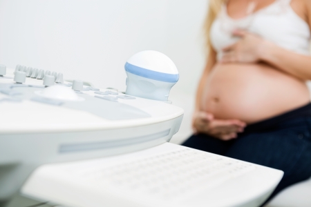 Closeup of ultrasound machine with pregnant woman in background at clinicの写真素材