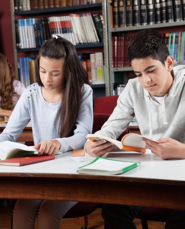 Teenage schoolchildren reading books at table in libraryの写真素材