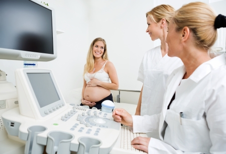 Gynecologists by ultrasound machine looking at pregnant woman in clinic