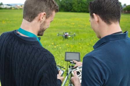 Rear view of young engineers with remote controls and screen operating UAV helicopter in park