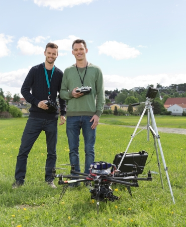 Happy young engineers standing by UAV helicopter and tripod in park