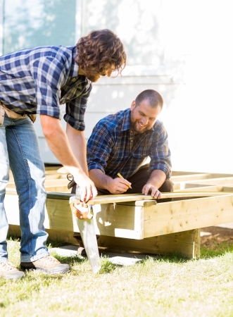Mid adult manual workers measuring wood at construction siteの写真素材