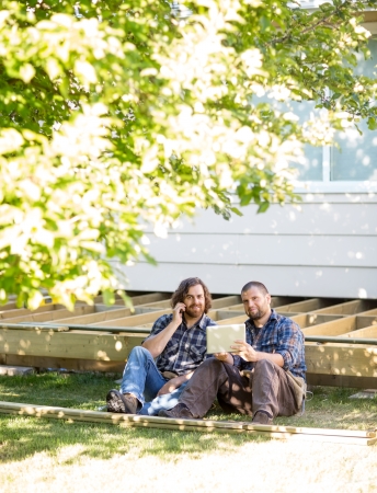 Portrait of mid adult manual workers using digital tablet and mobile phone at construction siteの写真素材