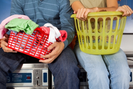 Midsection of young couple with laundry baskets sitting on top of washing machinesの写真素材