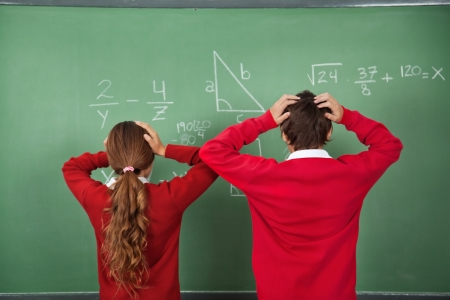 Rear view of confused schoolchildren standing against board in classroom