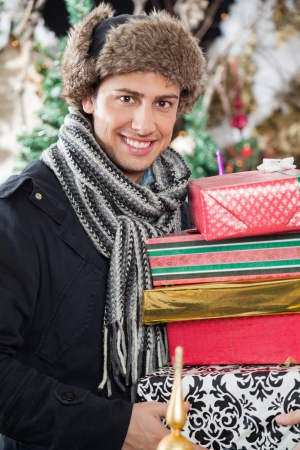 Portrait of happy young man carrying stacked gift boxes in storeの写真素材