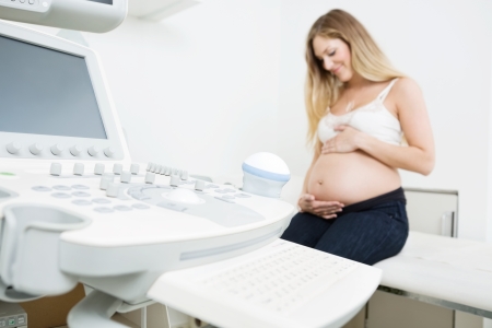 Pregnant woman holding tummy sitting by ultrasound machine in clinicの写真素材
