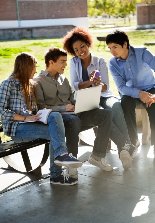 Full length of female student showing mobilephone to friends in college campusの写真素材