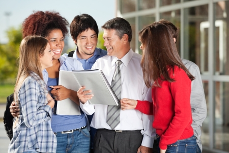 Happy students and teacher with book standing on university campusの写真素材