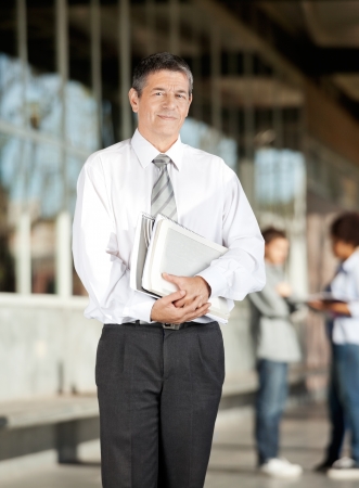 Portrait of mature male professor with book standing on university campusの写真素材