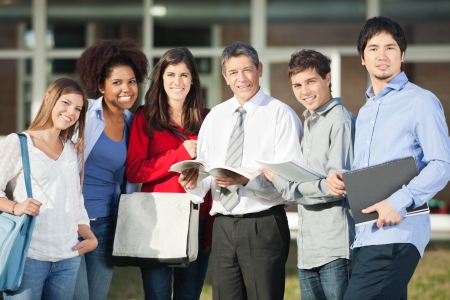 Portrait of confident male professor and students standing on university campusの写真素材