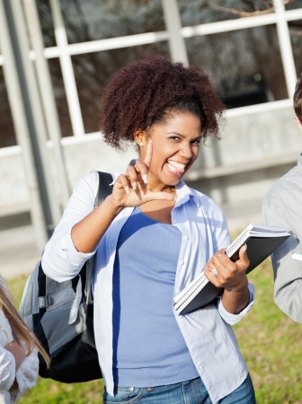 Portrait of playful female student holding books while gesturing loser sign on college campusの写真素材