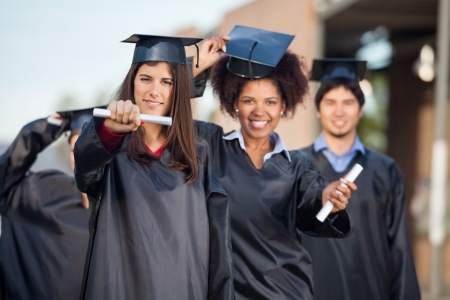 Portrait of confident female students showing certificates with friends in background on college campusの写真素材