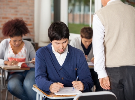 Group of students giving exam while teacher supervising them in classroomの写真素材