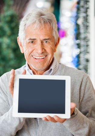 Portrait of happy senior man displaying digital tablet at Christmas storeの写真素材