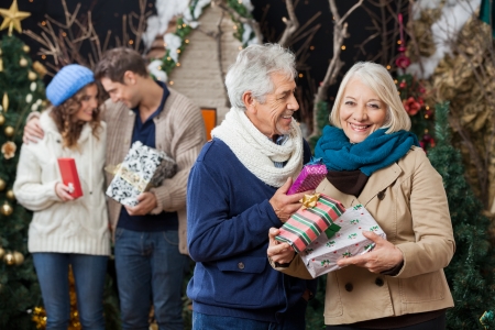 Portrait of happy senior couple holding Christmas presents with children standing in background at storeの写真素材