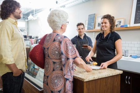 Portrait of confident male owner with colleagues and customers at cafe counter