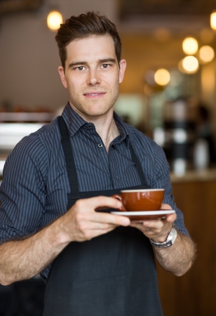 Portrait of barista holding cappuccino cup in cafeの写真素材