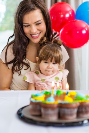 Happy mother with daughter celebrating birthday with cake on tableの写真素材