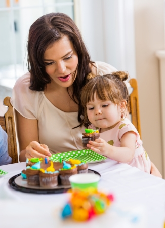 Mid adult mother with girl eating cupcake at birthday partyの写真素材