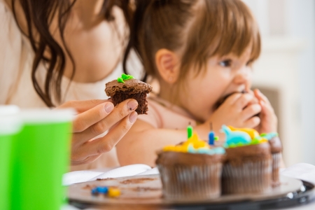 Cropped image of mother holding cupcake with girl eating cake at birthday partyの写真素材