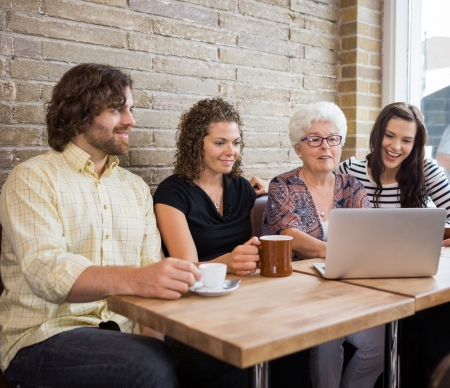 Senior woman with friends using laptop at table in cafeの写真素材