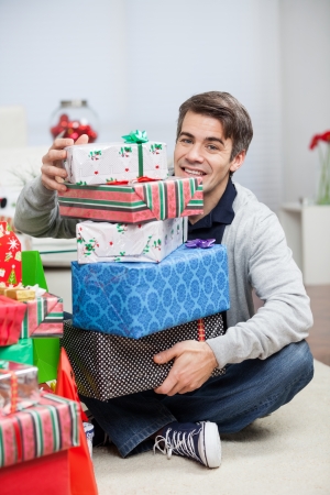 Full length portrait of happy mid adult man with stack of Christmas presents sitting on floor at homeの写真素材